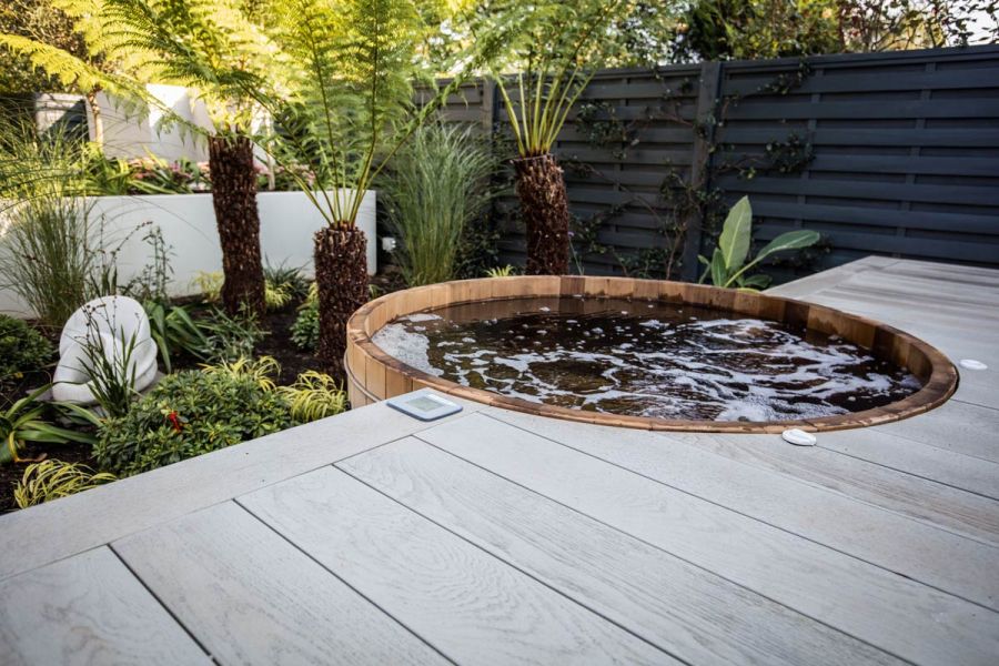 Millboard Smoked Oak composite deck laid flush with edge of water-filled half-barrel that juts out over low bed with tree ferns.