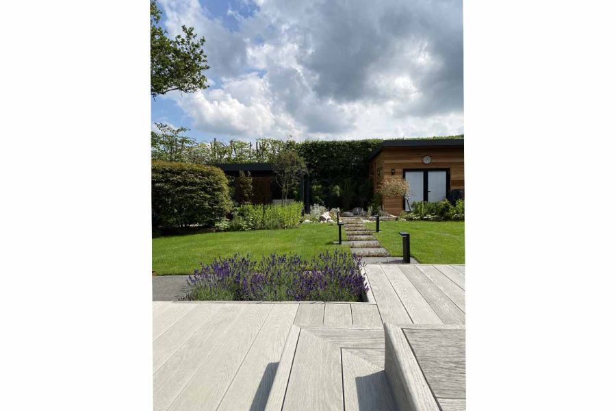 Low view from wrap-around step down to Smoked Oak Millboard composite decking above lawned garden. Design by David Keegan.