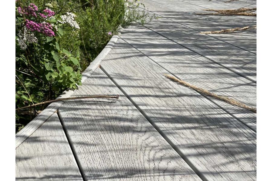 Edge of path of Millboard Smoked Oak composite decking, showing plank ends cut to curve of edging. Design by Martyn Wilson.