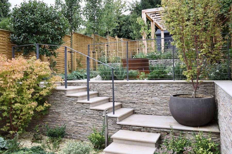 Bullnose steps leading to elevated patio area featuring Jura Beige smooth limestone complemented by lush planting and cobblestone cladding.