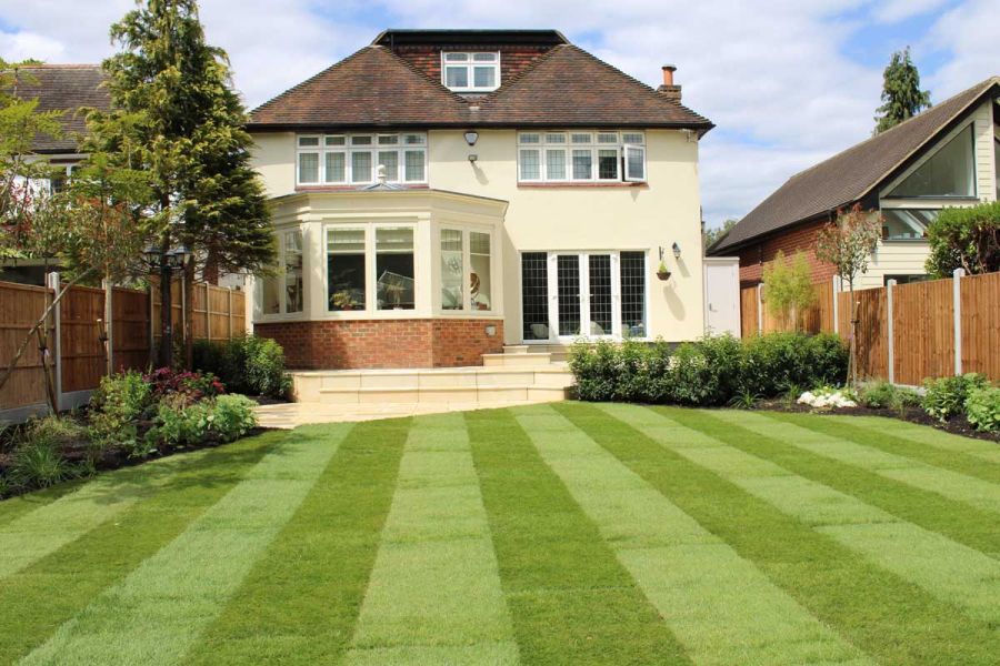 Striped lawn leads towards patio of Harvest sawn sandstone, with matching bullnose steps rising to cream-painted house.