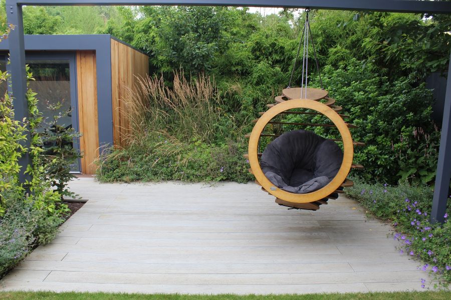 Bespoke wooden hanging chair suspended over Smoked Oak Millboard decking with deep naturalistically planted border on 2 sides.