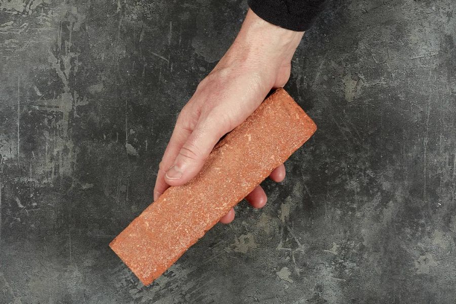 A hand holds a single orange-red Spalding clay paver against a dark background. Free UK next-day delivery available. 