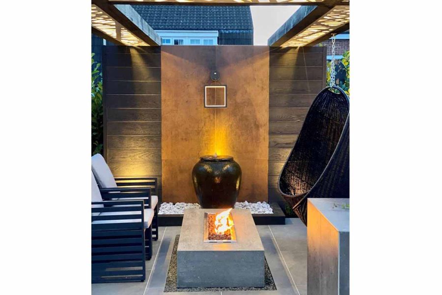 Giant glazed pot sits on white gravel between wall faced with Steel Corten external cladding and oblong fire pit table.