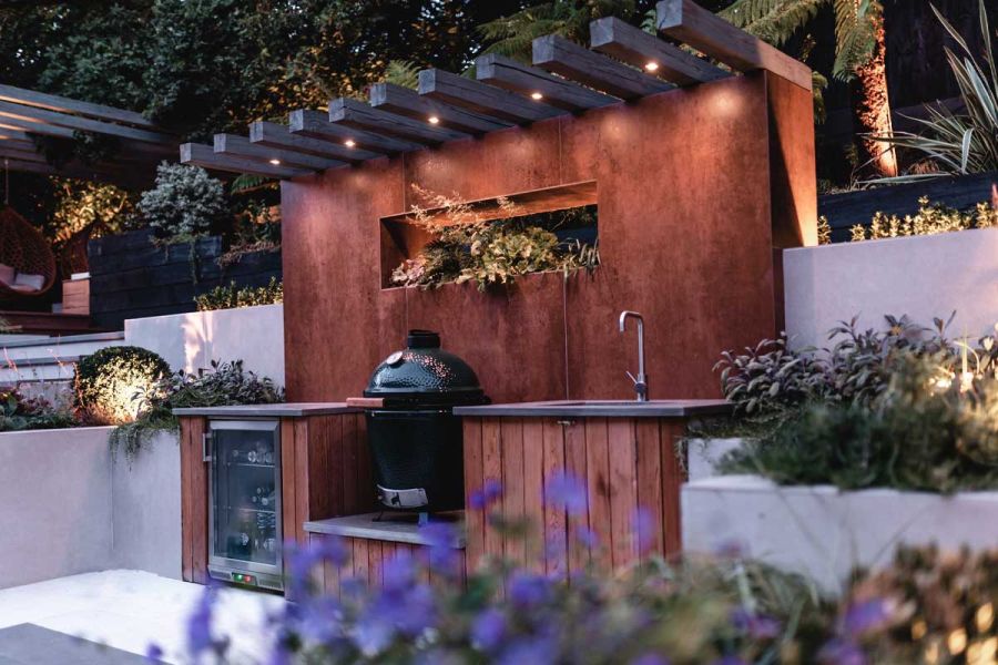 Outdoor kitchen with sink, wine cooler and barbecue, beneath large splashback faced with Steel Corten external cladding.