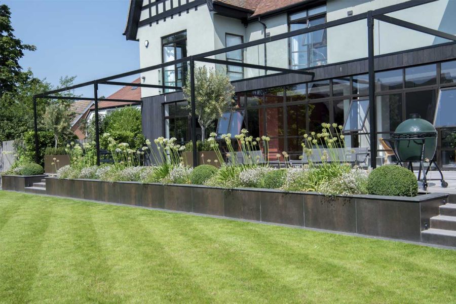 Pergola covered patio edged in retaining bed filled with structured planting and faced with Steel Dark DesignClad panels.