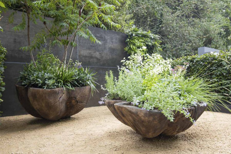 Organically shaped wooden planters on gravel and sand, next to tall wall faced with Steel Dark DesignClad external cladding.