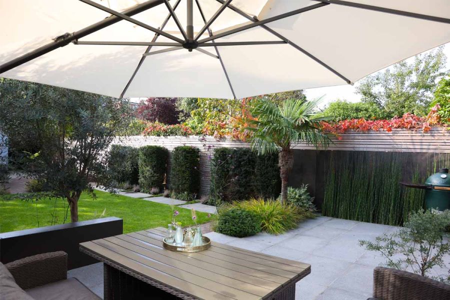 Modern garden design with metal garden furniture with parasol, featuring DesignClad Steel Dark external cladding to the right