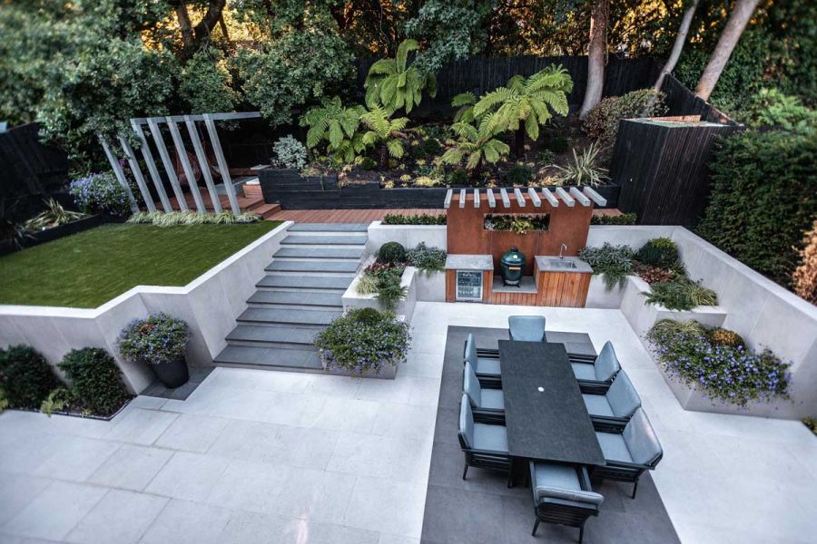 Steel Grey porcelain steps with white flanking walls rise from light paving to deck and lawn area. Design by Gardens of the Future.