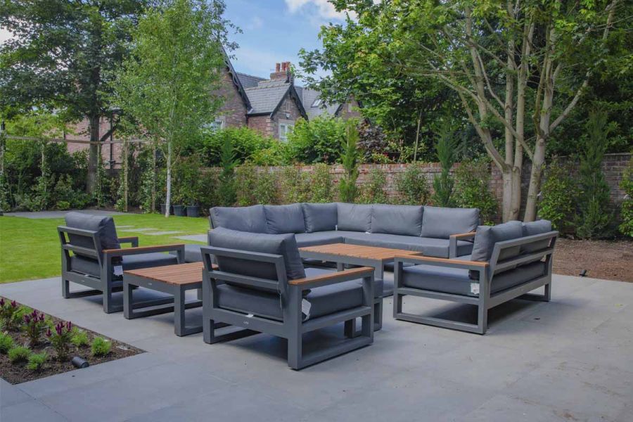 Large luxury garden furniture set, with corner sofa, on Steel Grey Porcelain patio, with trees and shrubs lining the fence behind.