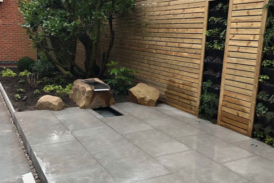 Small Steel Grey Porcelain patio with a boulder water feature to one side and a bespoke timber screen broken up with sections of living wall.