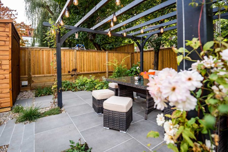 Steel Grey porcelain patio with brown wicker table and chairs and a timber garden structure over the top.