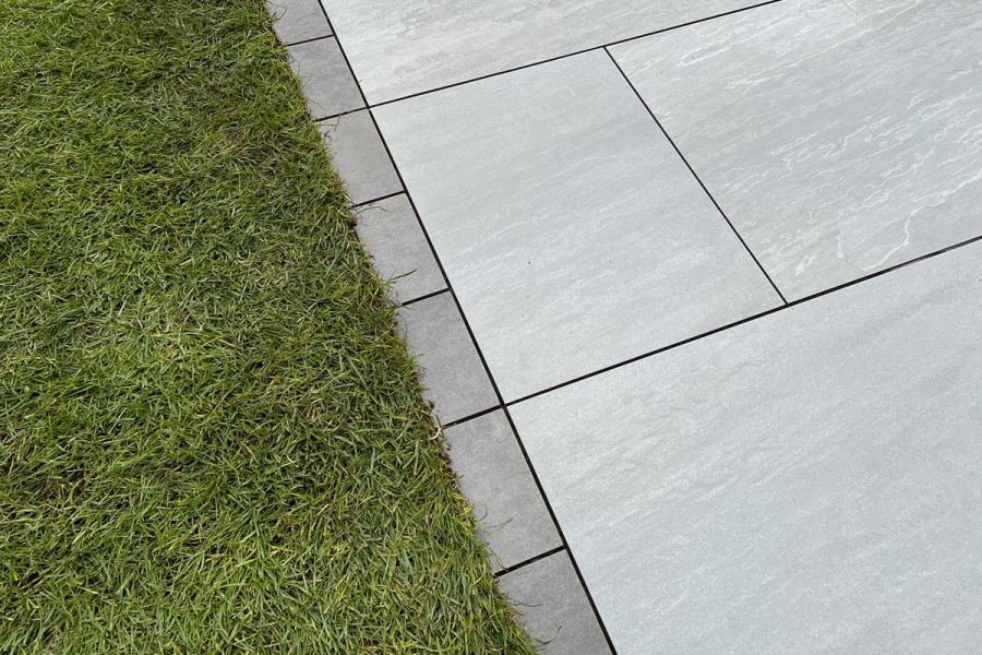 Close view of Steel Grey porcelain setts with dark grouting creating edge between pale paving and lawn. Built by Green Life.