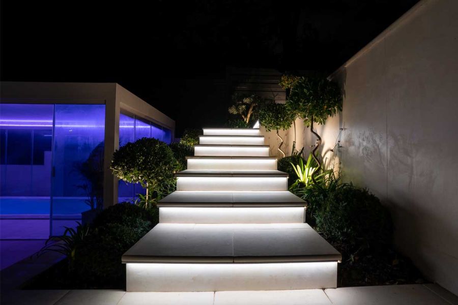 Deep, wide steps with Venetian beige bullnose porcelain treads with underlighting rise between high wall and class building.