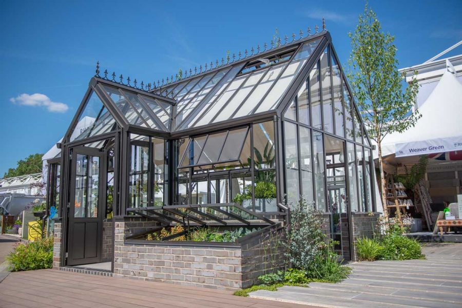 Victorian-style glasshouse with coldframes on one side of entrance and area decked with Chestnut Brushed Designboard in front.