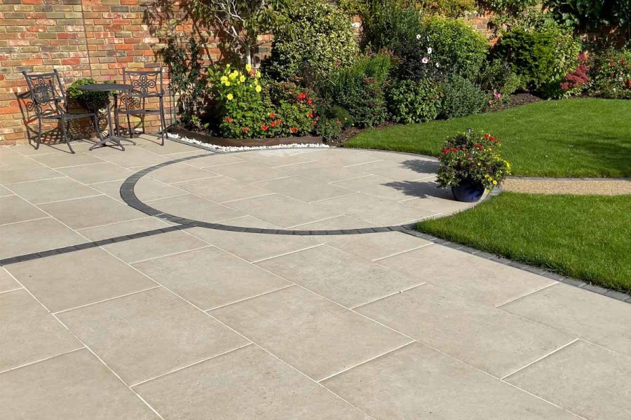 Florence Beige porcelain patio by Stokes Baldock Landscaping, with detailing In dark setts, lawn and flower border to right.