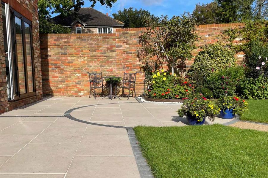 Florence Beige porcelain patio, with edging and circle outline in dark setts, in corner of walled garden between house and lawn.