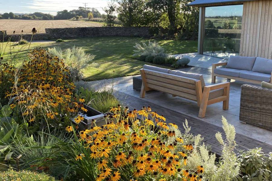 3 outdoor sofas on limestone paving edged with Stone Grey clay pavers in large lawned garden with uninterrupted view of fields.