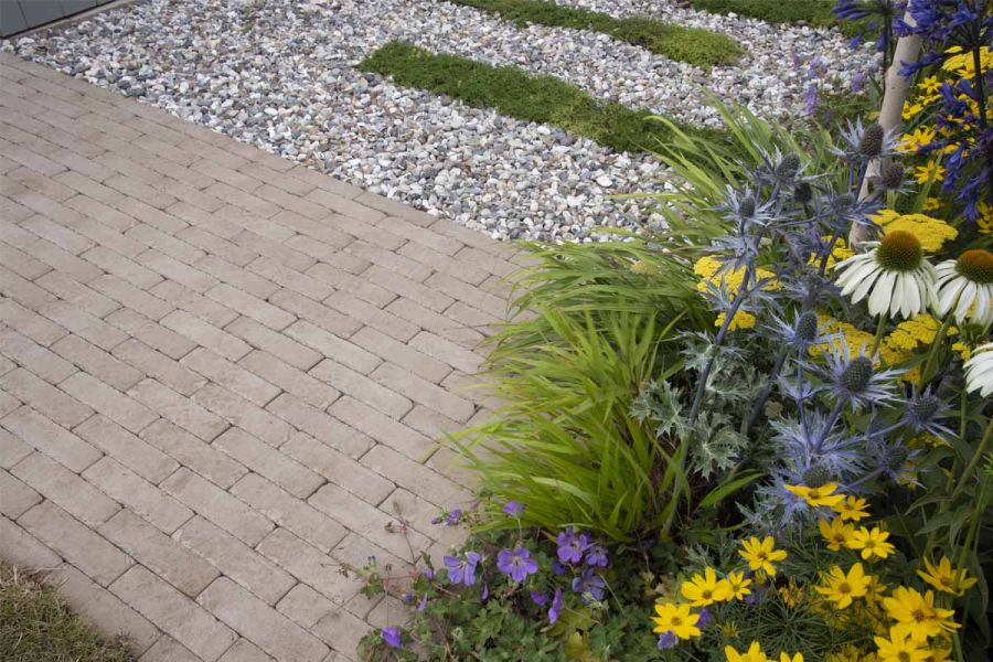 Close view of Stone Grey brick pavers between gravel and mauve and yellow planting. Design by Lynn Cordall. Built by mustard seed.