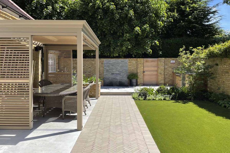 Wide strip of Stone Grey brick pavers, laid herringbone fashion with soldier course, divides Jura Grey patio dining area from lawn.