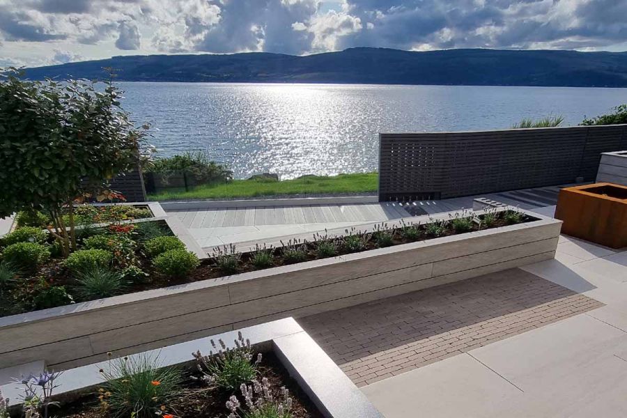 Rectangle of Stone Grey clay pavers next to timber raised bed in patio of light paving with view across open water to far shore.