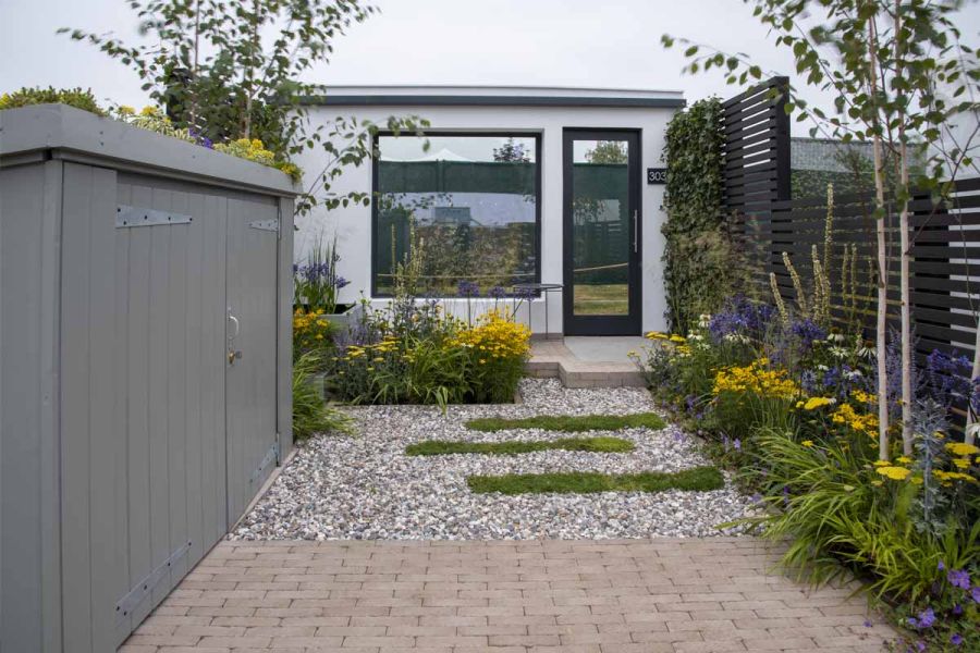 RHS Tatton Park show garden with yellow flowers, storage shed, gravel and Stone Grey clay pavers. Built by Mustard Seed Gardens.