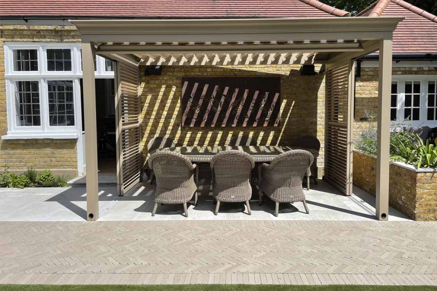 At the back of a bungalow, Stone Grey clay pavers edge limestone slabs of pergola-covered patio by Tom Howard Garden Design.