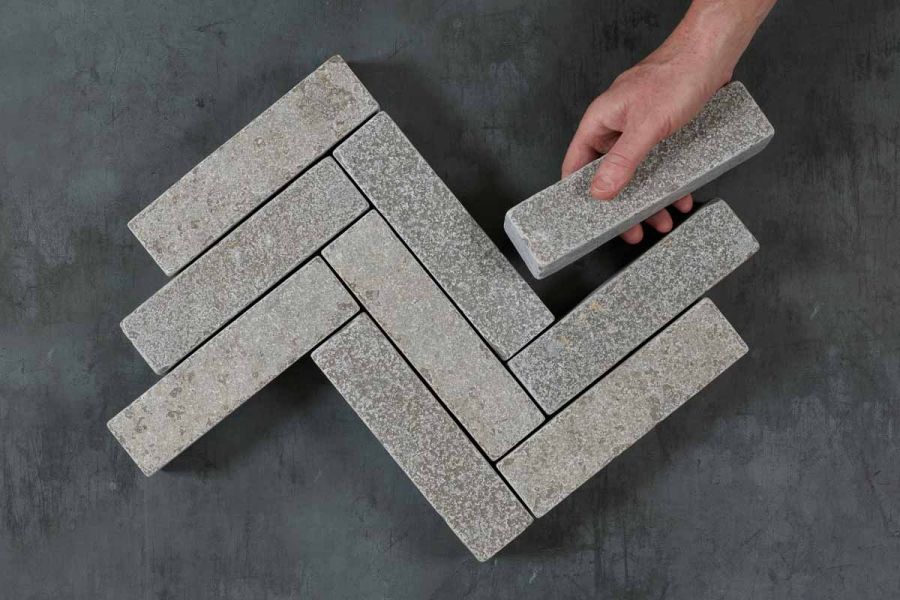 Hand places one Antique Grey limestone brick paver against 9 laid in 3 zigzag rows on dark background. Free UK delivery available.