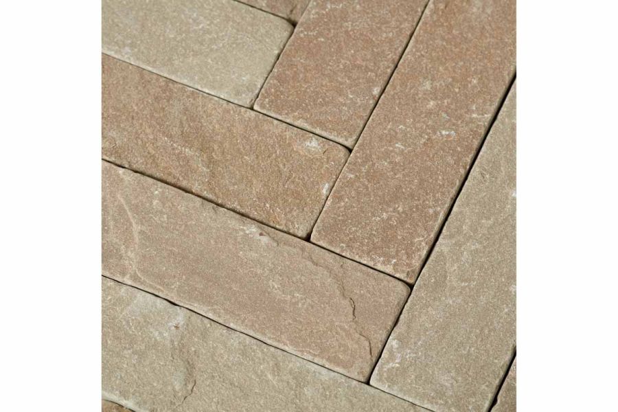 Close view of Raj Green tumbled sandstone pavers, laid herringbone, without mortar, showing riven surface and colour tones.