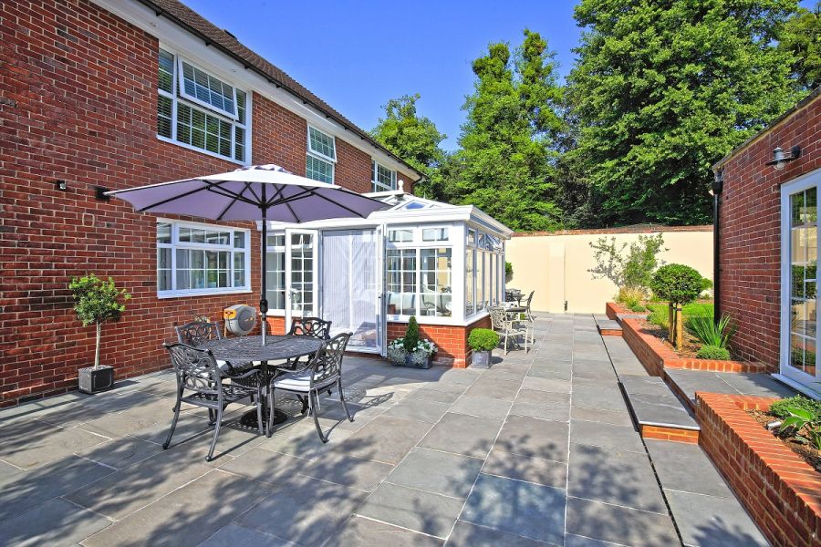 Metal dining set sits on patio of stone paving in Graphite Grey limestone running between back of house and brick building