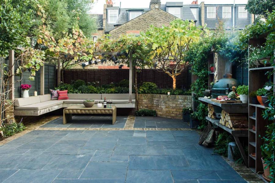 Small walled and fenced urban garden with inbuilt L-shaped bench and cooking area. Paved with Green slate stone slabs