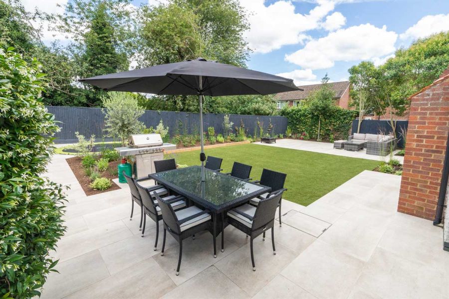 Family back garden with porcelain paved dining area, separate lounge seating zone, artificial lawn and sunken trampoline.