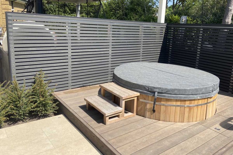 Hot tub on raised decking, bordered on 2 sides by screens of Dark Ash Composite timber battens. Designed by Thouvenin Landscapes.