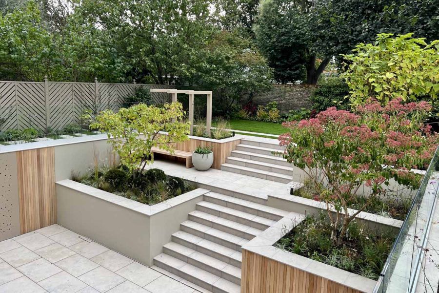 View down to terrace with Jura Grey porcelain garden steps descending to paving and ascending to to lawn. Design by Tom Howard.