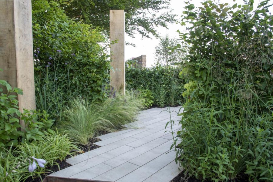 2 posts rise from bed planted with grasses next to path of Cream porcelain plank paving laid lengthwise on path by James Smith.