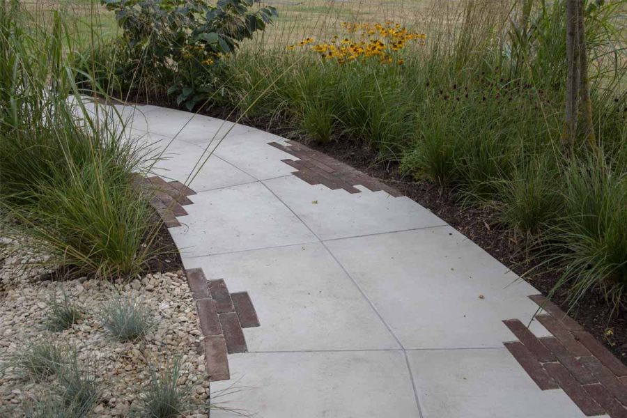 Curved path of Venetian Beige Porcelain bespoke paving slabs, inset with clay paver edge detail runs between planted beds.