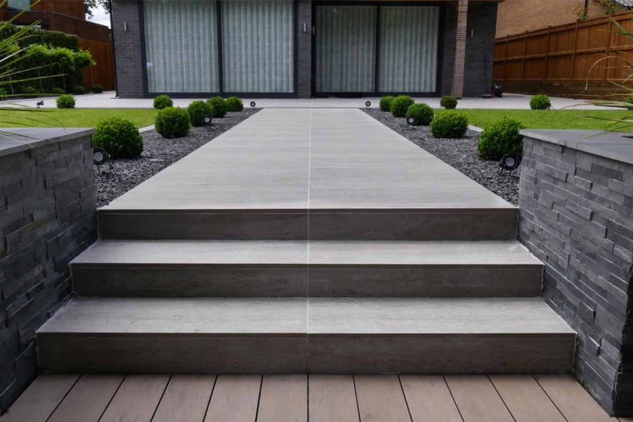 Traditional Designboard composite decking boards laid perpendicular to steps up to path leading between box balls to outdoor room.