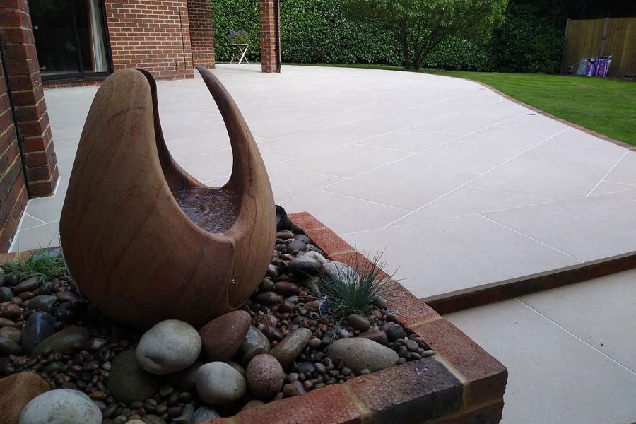 Florence Beige porcelain patio at back of house, paving slabs laid at angle by Transform Landscape Services. Water feature by step.