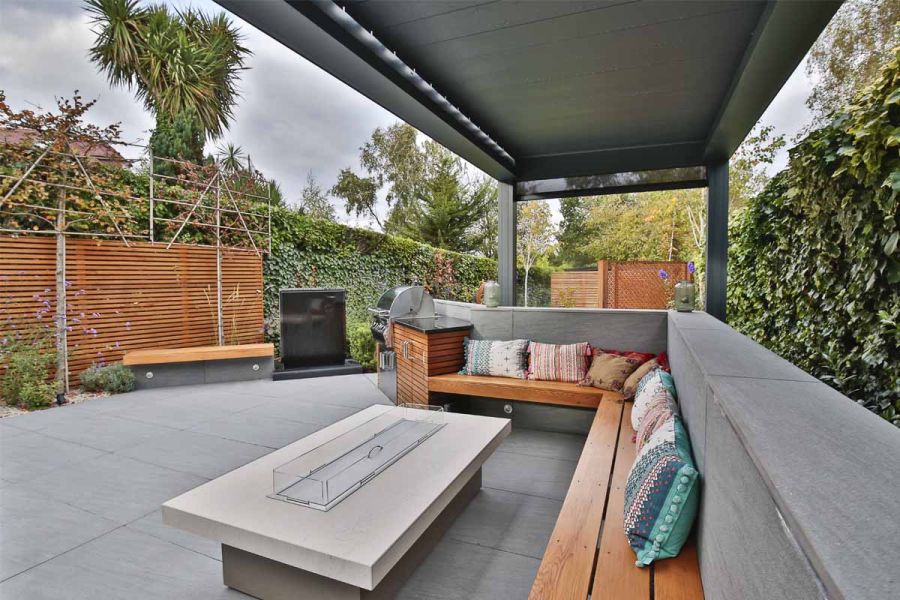 Firepit next to long benches cantilevered into walls faced with Trendy Black porcelain to match paving, covered by pergola.
