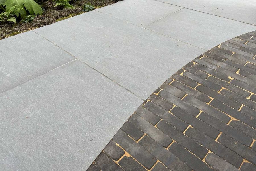 Light Grey Porcelain paving slabs cut to fit around a curved section of Charcoal Grey Clay Pavers.
