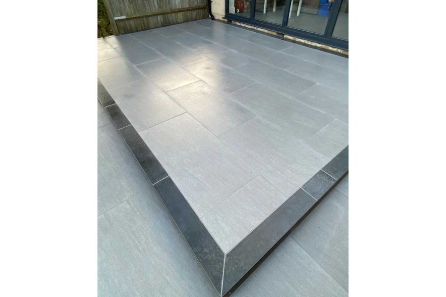 Trendy Black Porcelain Paving edges light grey patio tiles of raised area by glass doors. Built by Smith & Varney Landscapes.
