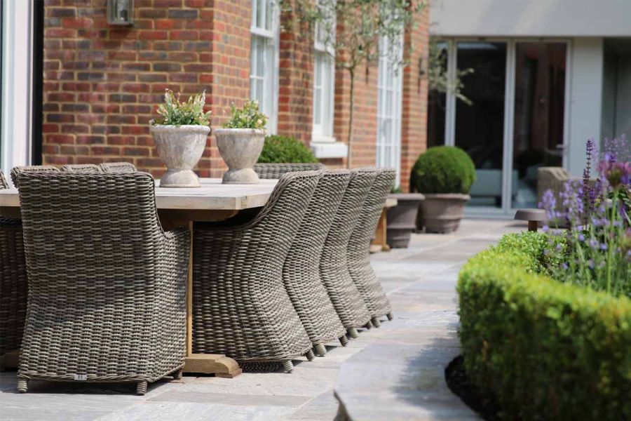 Dining set sits on Black Tumbled Indian sandstone paving at back of brick house with Georgian windows and modern extension.