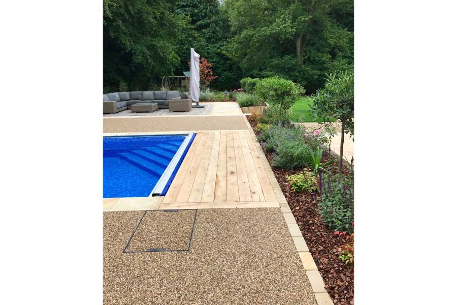 Tumbled Mint Sandstone Setts line swimming pool surround of resin-bonded gravel and decking. Modular lounge set in background.