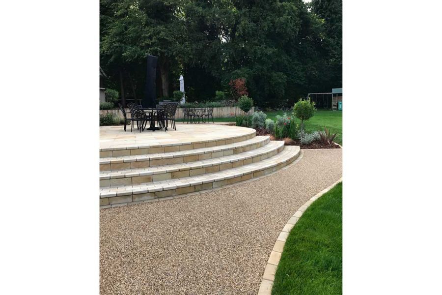 Tumbled Mint Sandstone Setts line resin-bonded gravel path passing curved flight of 4 steps up to patio with garden furniture.
