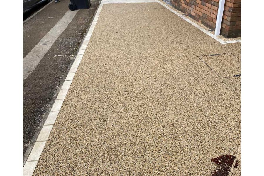 Between brick wall and strip of earth lies a resin-bound gravel path edged with small cream porcelain patio tiles.