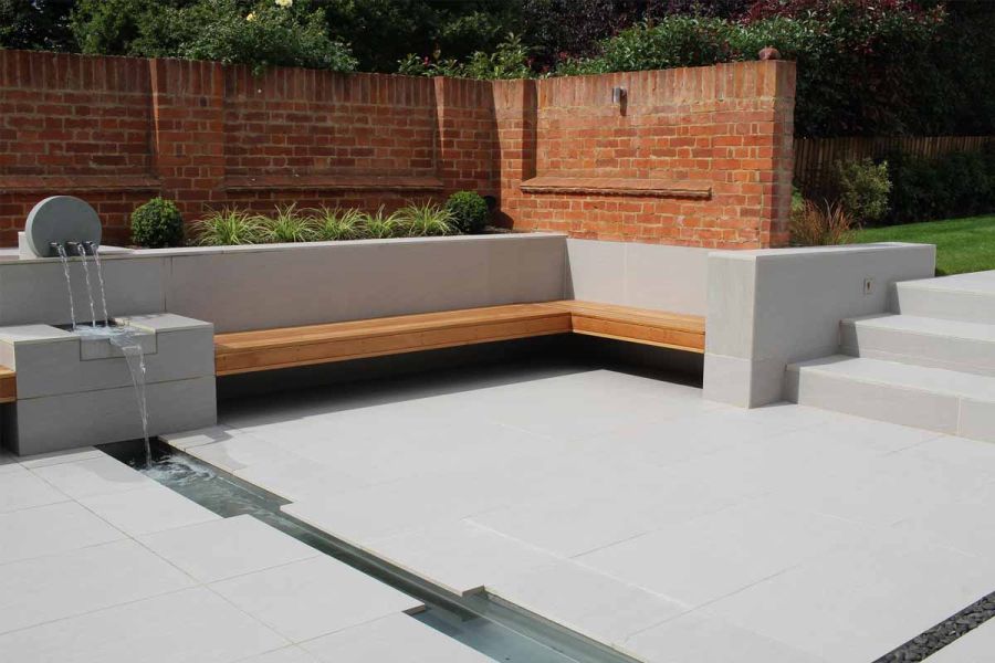 Sunken seating area paved in Urban Grey 20mm outdoor porcelain tiles. A  water feature spills into rill that runs across paving.