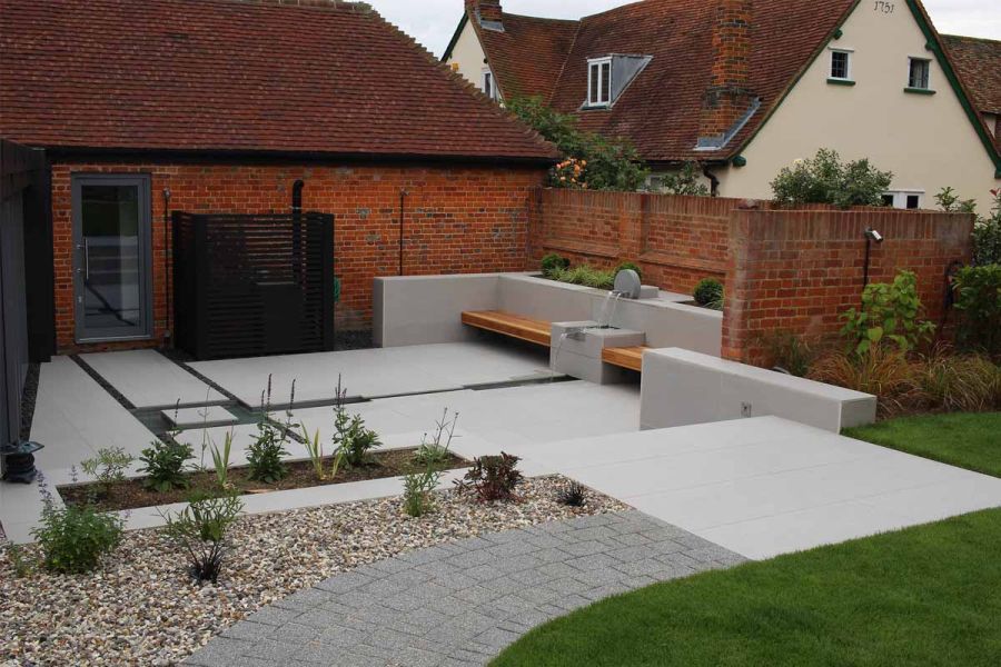 Curved path leads to Urban Grey porcelain paved landing at top of steps down to paved courtyard water feature and bench seating.