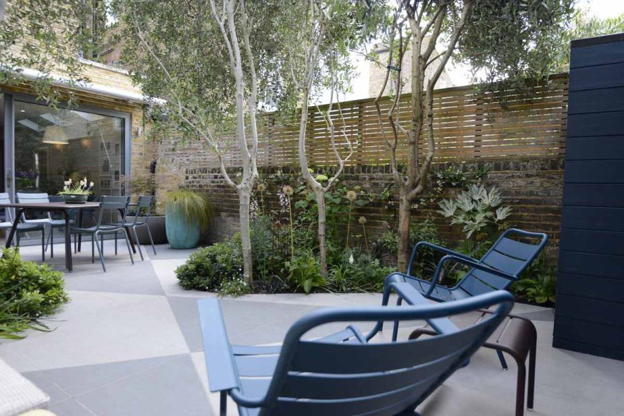 Sleek courtyard garden using trendy black and urban grey porcelain tiles in angular patterns, complemented by fencing and trees for privacy.