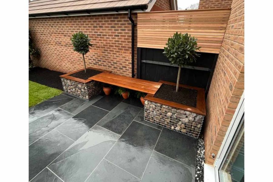 Planter bench of wood and gabions sits against wall and fence at one end of Brazilian black slate patio at back of modern house.