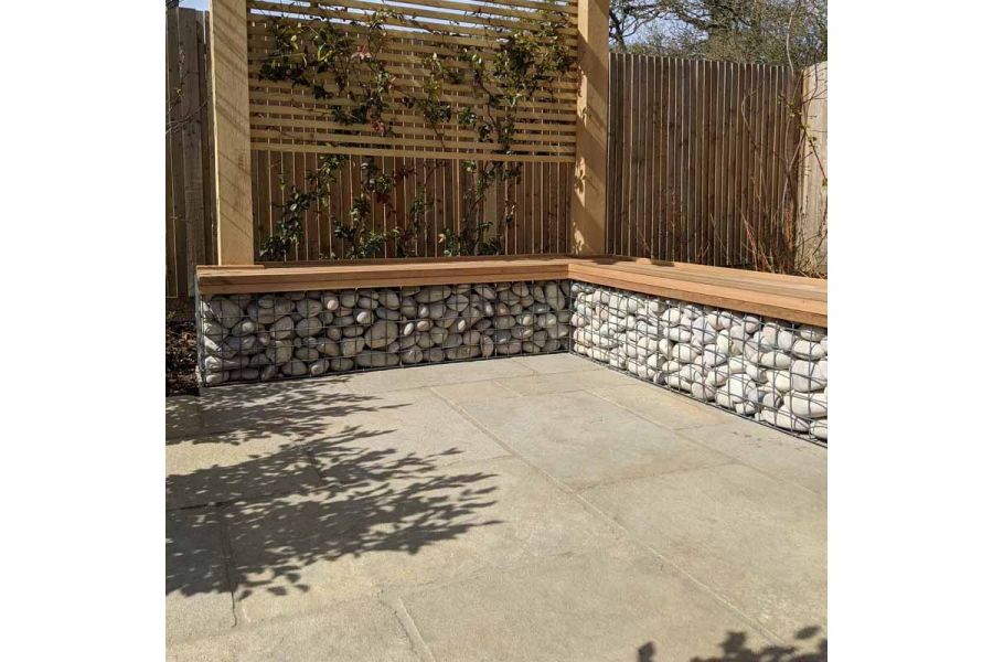 Shadows fall on small Antique Yellow limestone patio with stone-filled gabions on 2 sides forming wood-topped bench.